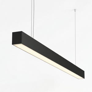 Può includere: Una moderna lampada a sospensione nera di forma rettangolare con un pannello luminoso bianco brillante. La lampada è sospesa al soffitto tramite sottili cavi argentati. Il design è minimalista, adatto a vari stili di interni.