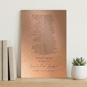 May include: A copper-colored metal plaque with engraved text. The plaque features a song's lyrics arranged in a vertical pattern. Below the lyrics, it reads "OUR FIRST DANCE, November 12, 2025" and the names "Lance & Maria Angelina".