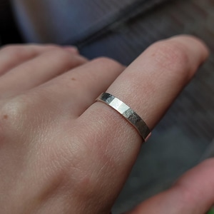 Op de afbeelding: Een zilveren ring met een getextureerde, gehamerde afwerking. De ring wordt aan een vinger gedragen.