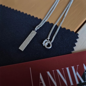 Collar con colgante de estructura minimalista de plata fundida con forma rectangular y alargada.