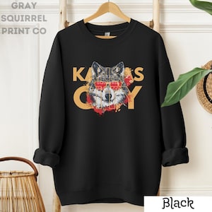 May include: Black sweatshirt with a wolf graphic and the text "KANSAS CITY" in yellow and red. The wolf is wearing red sunglasses.