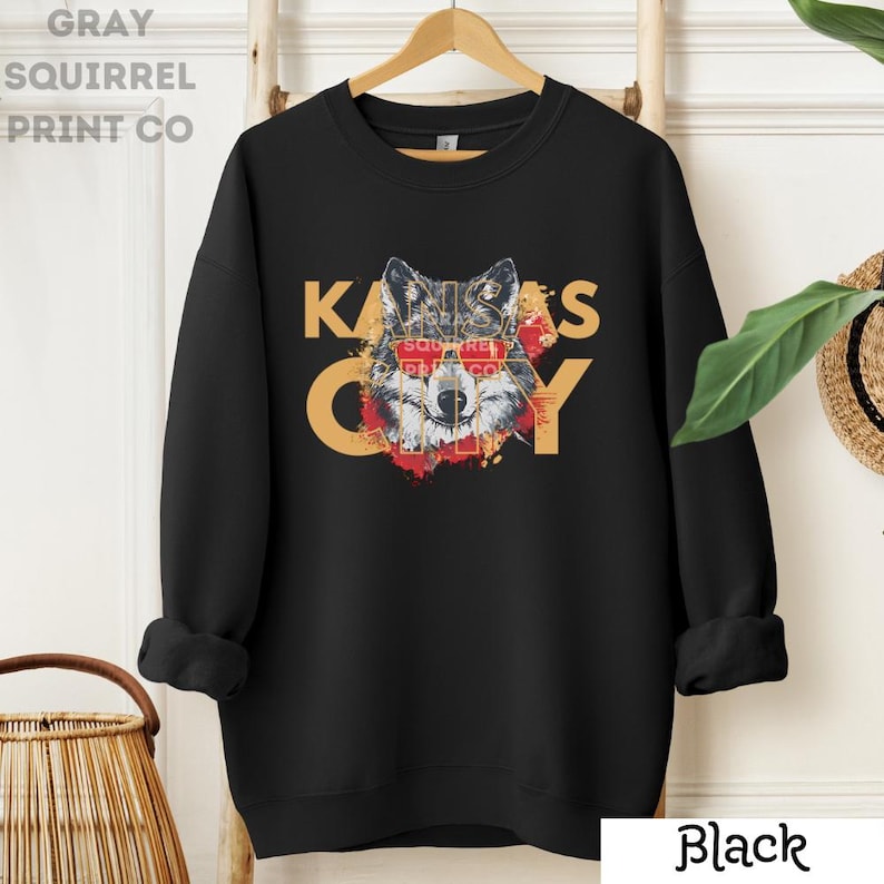 May include: Black sweatshirt with a wolf graphic and the text "KANSAS CITY" in yellow and red. The wolf is wearing red sunglasses.