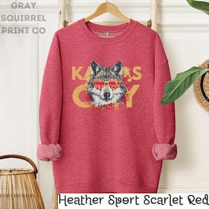 May include: Heather Sport Scarlet Red sweatshirt with a wolf wearing sunglasses and the text "KANSAS CITY" in yellow.