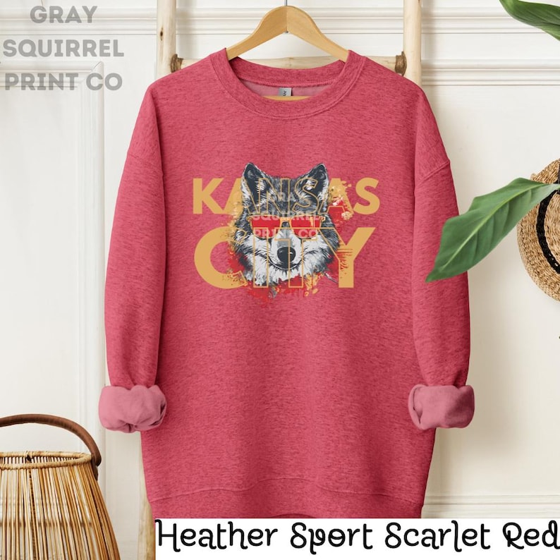 May include: Heather Sport Scarlet Red sweatshirt with a wolf wearing sunglasses and the text "KANSAS CITY" in yellow.