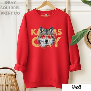 May include: Red sweatshirt with a wolf graphic and the text "Kansas City" in yellow letters. The wolf's eyes are covered by a red banner with the text "Gray Squirrel Print Co."