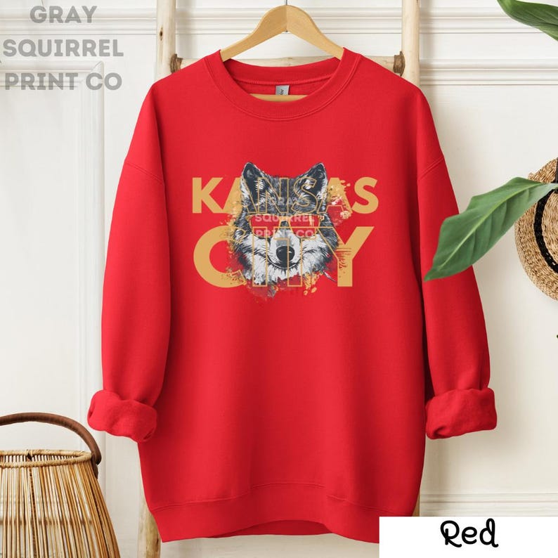May include: Red sweatshirt with a wolf graphic and the text "Kansas City" in yellow letters. The wolf's eyes are covered by a red banner with the text "Gray Squirrel Print Co."