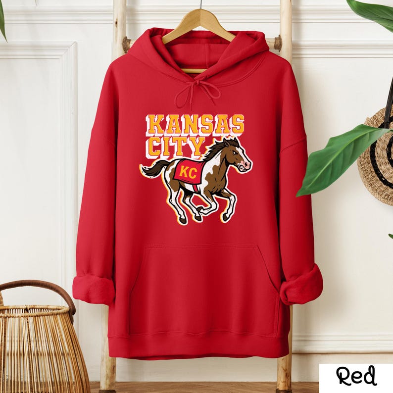 May include: A red hooded sweatshirt with a graphic of a horse and the words "Kansas City" in yellow and white. The horse has brown and white markings and a red saddle with "KC" on it.