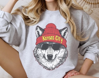 May include: Gray sweatshirt with a graphic of a wolf wearing a red beanie with the text "Kansas City" on it. The wolf is wearing sunglasses.