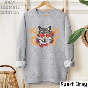 May include: A gray sweatshirt with a wolf wearing sunglasses and the text "KANSAS CITY" in gold letters. The wolf is surrounded by a red and yellow paint splatter.
