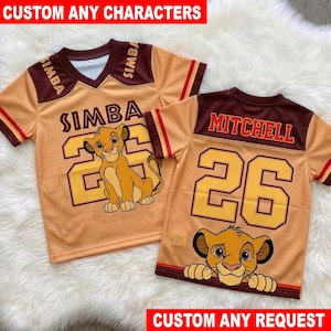 May include: Two tan and brown V-neck jerseys featuring mesh fabric. The left jersey displays the name SIMBA, the number 26, and a lion cub graphic. The right jersey shows the name MITCHELL, the number 26, and a lion cub face graphic.