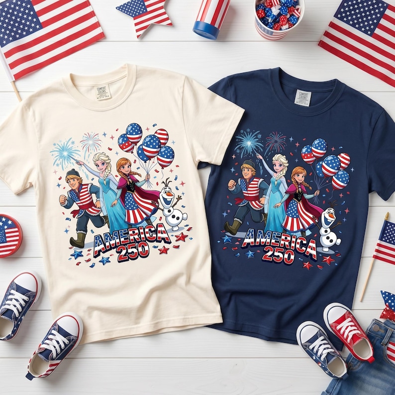 K&ouml;nnte beinhalten: Zwei kurz&auml;rmelige T-Shirts, eines in Creme und eines in Marineblau, mit einem Grafikdruck von drei animierten Figuren und einem Schneemann. Das Design zeigt US-Flaggenmuster, Luftballons, Feuerwerk und den Schriftzug "AMERICA 250" in Rot, Wei&szlig; und Blau.