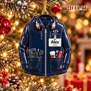 May include: A navy blue hoodie ornament featuring a pair of black headphones, a white ID badge labeled Alex 2026, and a code snippet graphic. The pockets contain a smartphone, a stylus, glasses, a coffee cup, a USB drive, and a red energy drink.