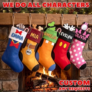 May include: Five personalized Christmas stockings hanging in a row. The first is blue with a white cuff labeled EMMA, a red bow, and a ship. The second is yellow with a brown cuff labeled MIA and dog ears. The third is orange with a green cuff labeled AMELIA and a green hat. The fourth is red with a black cuff labeled EVELYN and white gloves. The fifth is pink with white polka dots, a black cuff labeled OLIVIA, and a pink bow.
