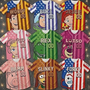 Op de afbeelding: Negen honkbalshirts met personages uit Toy Story. Elk shirt toont het gezicht van een personage aan &eacute;&eacute;n kant, met de naam van het personage en het nummer "00" aan de andere kant. De kleuren zijn onder meer blauw, rood, geel, roze en groen.