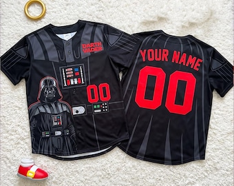Puede incluir: Una camiseta de béisbol negra con botones que presenta un gráfico de Darth Vader en la parte delantera con detalles en rojo y el texto "DARTH VADER". La parte trasera muestra el texto "YOUR NAME" y el número "00" en fuente roja grande.