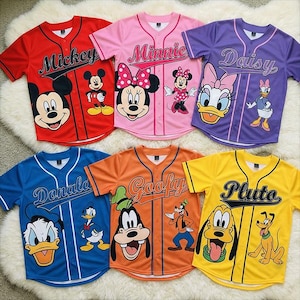 May include: Six baseball-style jerseys in red, pink, purple, blue, orange, and yellow. Each jersey features a Disney character's name and image: Mickey, Minnie, Daisy, Donald, Goofy, and Pluto. The jerseys have white trim and button closures.
