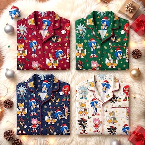 May include: Four button-down pajama shirts in red, green, navy blue, and white, each featuring a repeating pattern of Sonic the Hedgehog characters wearing Santa hats, interspersed with gold snowflakes and holly berries.