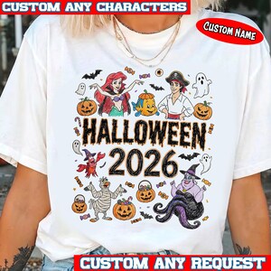 May include: A white t-shirt featuring a colorful graphic print with the text HALLOWEEN 2026. The design includes cartoon characters, pumpkins, ghosts, bats, and candy. The shirt also displays the text CUSTOM ANY CHARACTERS and CUSTOM NAME.
