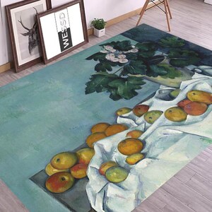 May include: A blue and green rug with a painting of a still life featuring a white cloth, yellow apples, and a green plant in a vase.