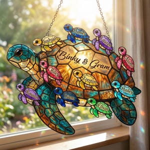 May include: Stained glass turtle suncatcher with the names of family members. The turtle is in shades of blue, green, and gold, with smaller turtles in various colors. The text "Binky & Gram" is displayed on the turtle's shell.
