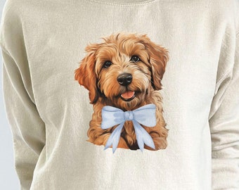 May include: A beige sweatshirt with a brown and white dog wearing a blue bow tie printed on the front. The sweatshirt has long sleeves and a crew neck.
