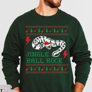 May include: A dark green Christmas sweater with a white and black snake design. The sweater has the text "Jingle Ball Rock" and a red lightning bolt on the front.