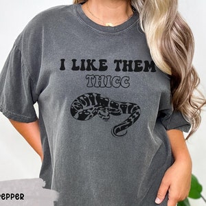 May include: A gray t-shirt with the text "I like them THICC" in black, featuring a black and white snake graphic.