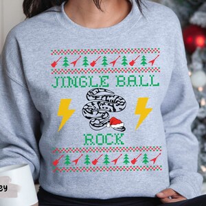 May include: A gray sweatshirt with a Christmas-themed design featuring a snake wearing a Santa hat and the text "Jingle Ball Rock".