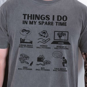 May include: A gray t-shirt with the text "THINGS I DO IN MY SPARE TIME" and a series of illustrations depicting activities related to ball pythons. The illustrations include dreaming about ball pythons, handling ball pythons, researching ball pythons, feeding ball pythons, buying ball pythons, and talking about ball pythons.