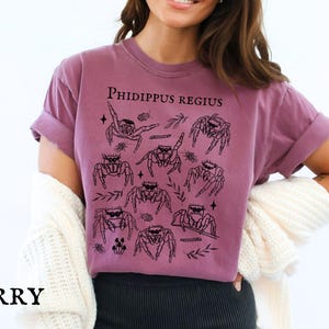 Pu&ograve; includere: T-shirt color bacca con grafica nera di ragni saltatori e la scritta "Phidippus Regius". La maglietta ha maniche corte e una vestibilit&agrave; rilassata. La parola "BERRY" &egrave; stampata in basso.