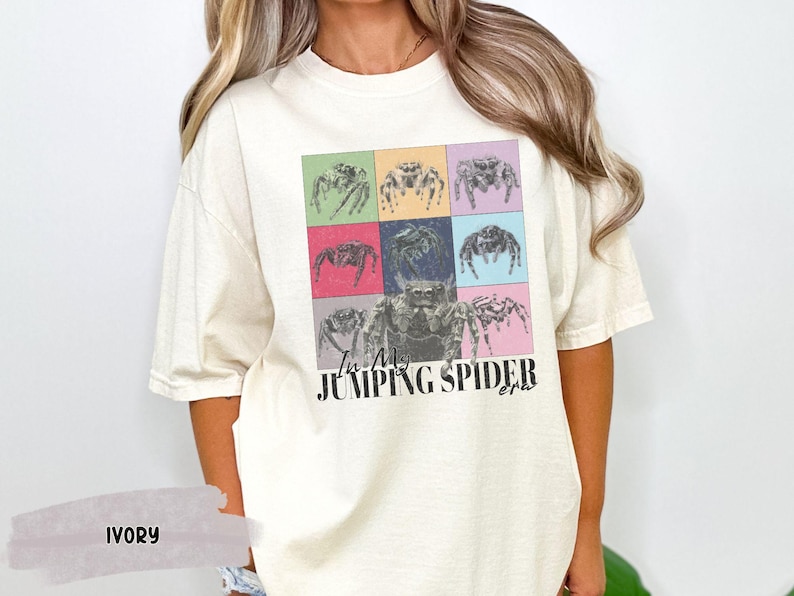 Op de afbeelding: Een wit T-shirt met een kleurrijke afbeelding van springende spinnen en de tekst "I'm a Jumping Spider girl".