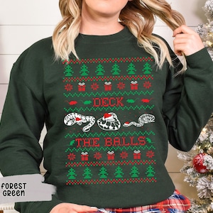 May include: A forest green Christmas sweater with a white, red, and green pattern. The sweater features a snake with a Santa hat and the text "Deck the Balls".