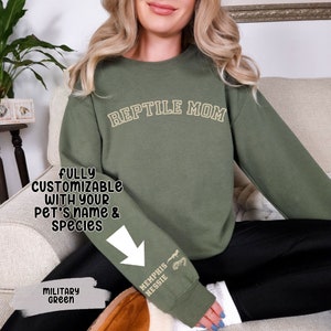 May include: A green sweatshirt with the text "REPTILE MOM" in gold lettering. The sweatshirt is fully customizable with your pet's name and species. The sleeve has a gold graphic of a lizard and the text "MEMPHIS NESSIE".