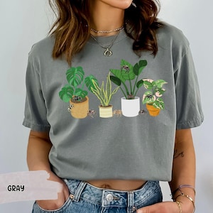May include: Gray t-shirt with a graphic of potted plants and spiders. The shirt has a crew neck and short sleeves.
