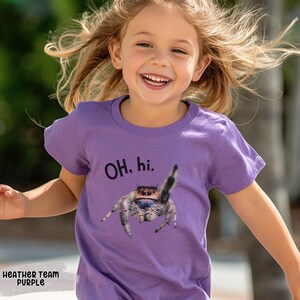 May include: A young child wearing a purple t-shirt with a jumping spider graphic and the text "OH. hi." printed on it.
