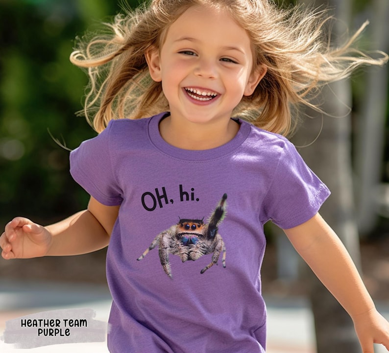 May include: A young child wearing a purple t-shirt with a jumping spider graphic and the text "OH. hi." printed on it.