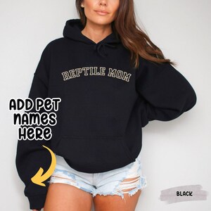 May include: Black hoodie with the text "REPTILE MOM" in gold lettering. The hoodie has a drawstring hood and a kangaroo pocket.