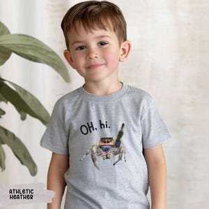 May include: A light gray t-shirt with a jumping spider graphic and the text "OH. hi." printed on the front. The shirt is made of a soft, comfortable material.
