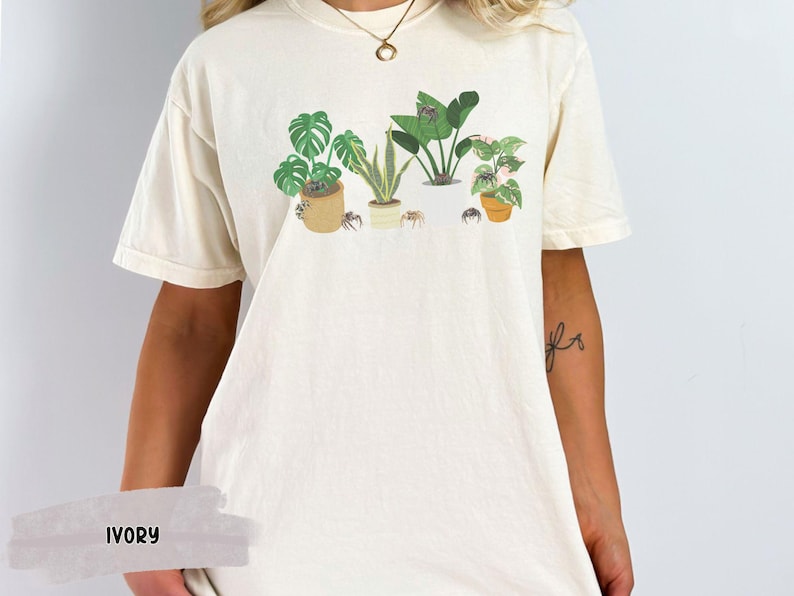 May include: A white t-shirt with a graphic of potted plants and spiders. The shirt is available in the color ivory.