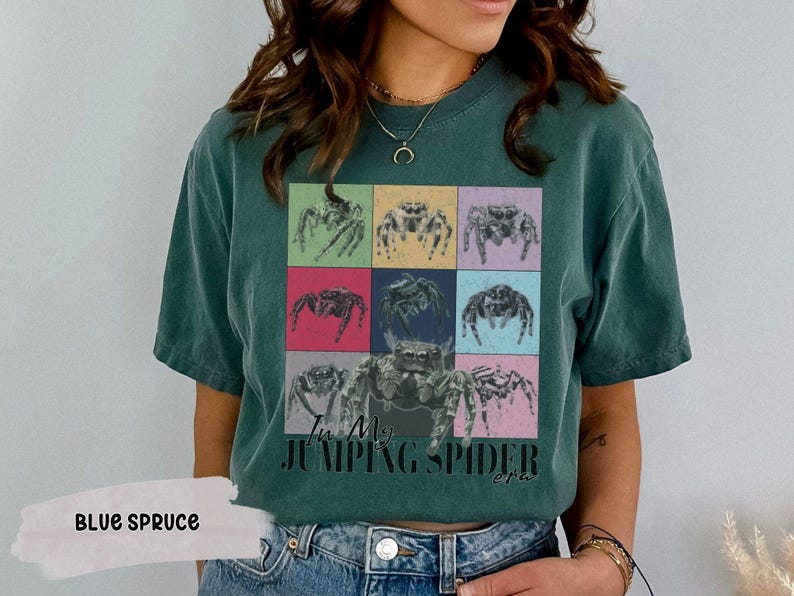 Op de afbeelding: Een donkergroen T-shirt met een kleurrijke afbeelding van springende spinnen en de tekst "I'm My Jumping Spider Era".