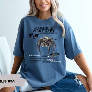 May include: A blue t-shirt with a graphic of a spider and the text "MULTI-LEGGED WEB PUPPY (PHIDDIPUS FRIENDLIEST)". The text also includes "ALSO KNOWN AS", "DANGER", and "FACT FILE" with additional information about the spider.