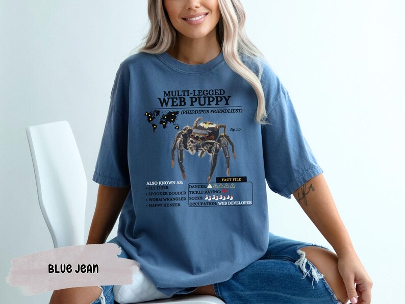 May include: A blue t-shirt with a graphic of a spider and the text "MULTI-LEGGED WEB PUPPY (PHIDDIPUS FRIENDLIEST)". The text also includes "ALSO KNOWN AS", "DANGER", and "FACT FILE" with additional information about the spider.
