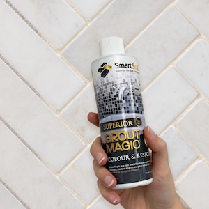 May include: A bottle of SmartSeal Superior Grout Magic colour and restorer. The bottle is white with a black and silver label. The text "SUPERIOR GROUT MAGIC" is displayed. The background is a white herringbone tile pattern.