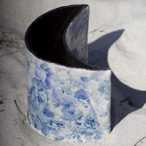 Pode incluir: Um vaso de cerâmica em forma de lua crescente, pintado em tons de azul e branco com um efeito de respingo.