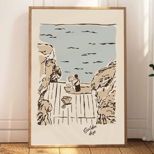 May include: A framed art print featuring a minimalist illustration of a person reading by the sea. The artwork uses a palette of beige, blue, and brown. The words "Golden days" are written in cursive at the bottom.