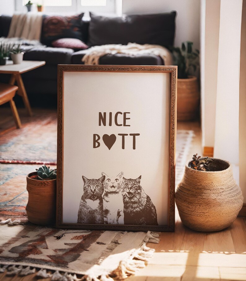 May include: A framed print with the text "NICE B♡TT" and a picture of three cats. The frame is brown wood with a decorative border.