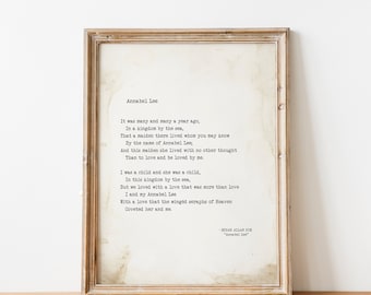 May include: A framed print of the poem "Annabel Lee" by Edgar Allan Poe. The poem is printed in a typewriter font on a textured, off-white paper. The frame is a simple, light wood.