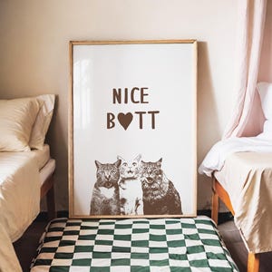May include: A white poster with a brown frame, featuring three cats with the text "NICE B❤TT" printed in brown.