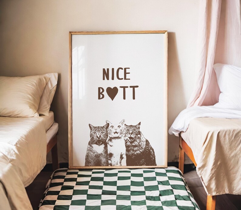 May include: A white poster with a brown frame, featuring three cats with the text "NICE B❤TT" printed in brown.