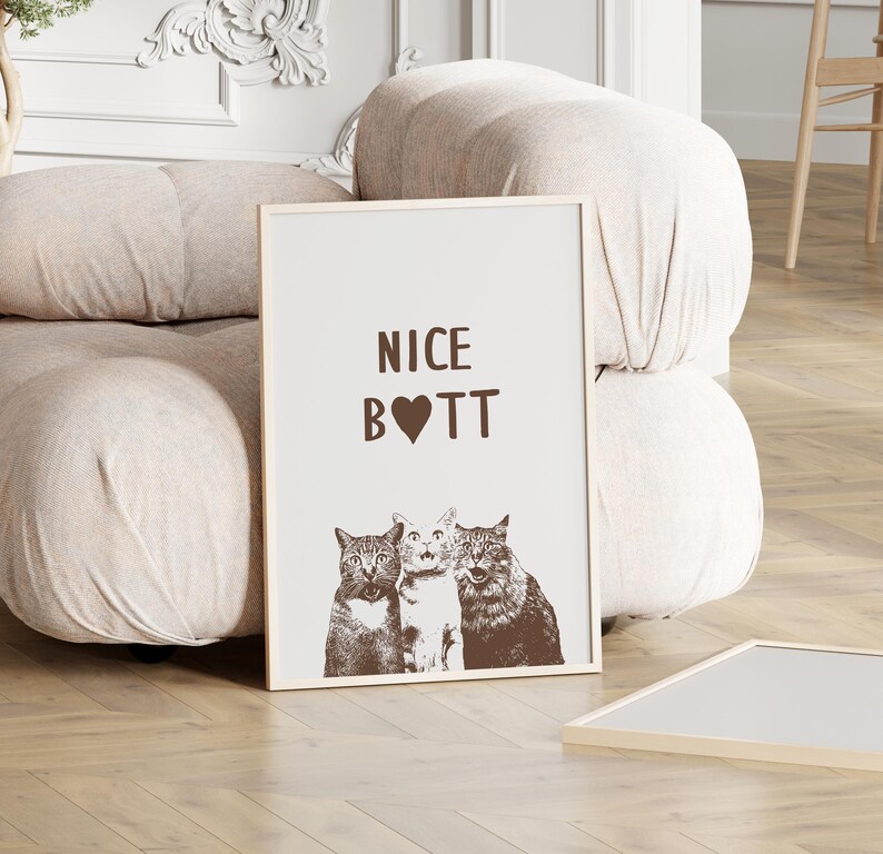 May include: A white framed print with the text "NICE BOTT" in brown lettering with a heart in place of the "O". Three cats are pictured below the text, two with their heads turned to the left and one with its head turned to the right.
